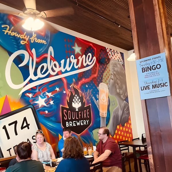 Patrons seated at tables in a brewery with a colorful mural and event signs on the wall.