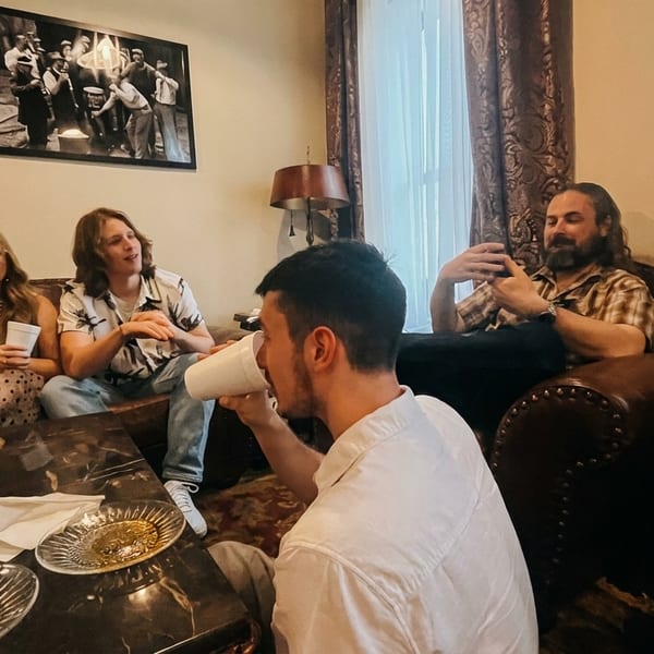 Five people relaxing on brown leather couches and chairs, chatting and drinking from white cups.