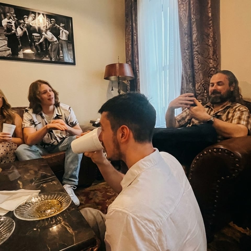 Five people relaxing on brown leather couches and chairs, chatting and drinking from white cups.