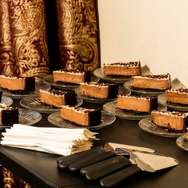 Numerous slices of chocolate cheesecake with white and dark chocolate drizzle on individual glass plates.
