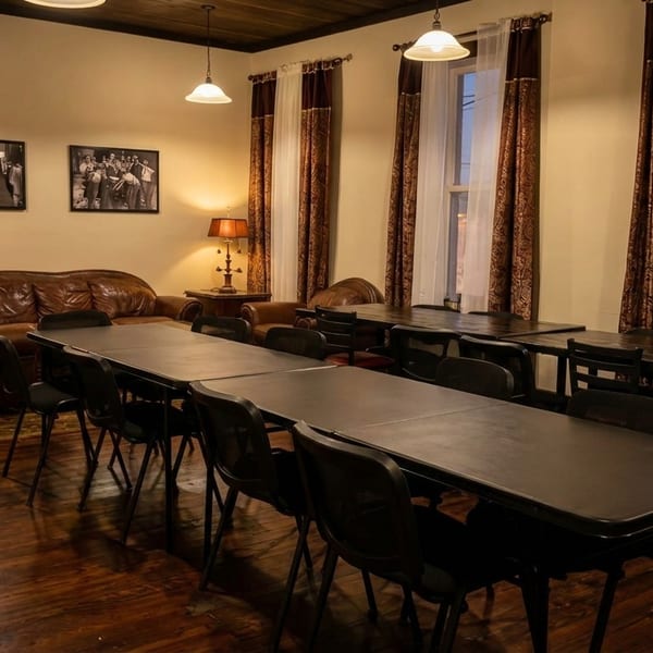A cozy restaurant interior with long tables and chairs, a leather sofa, and warm lighting.