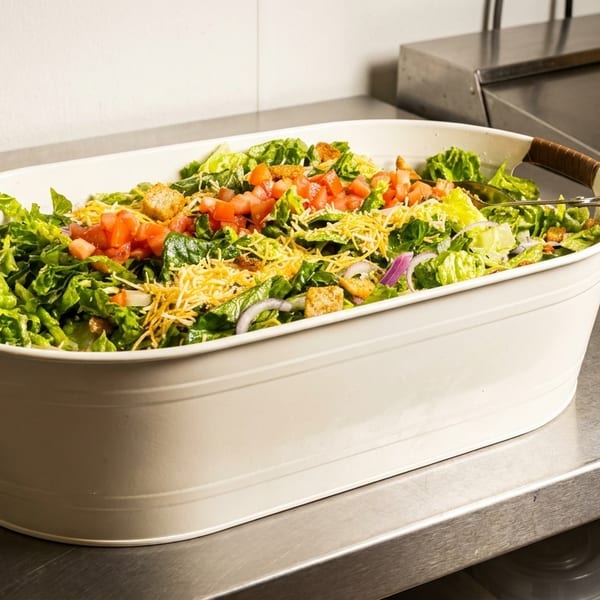 Large white serving tub filled with fresh green salad, topped with tomatoes, cheese, and croutons.