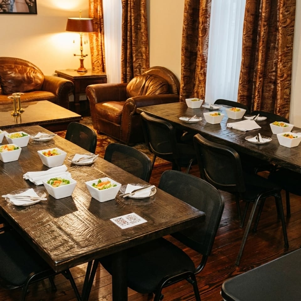 Restaurant dining room with two long wooden tables set with salads, and a lounge area with leather furniture.