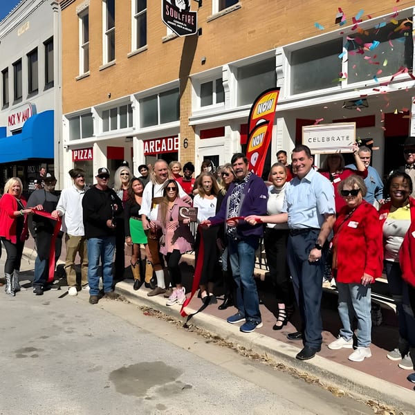 A group of people celebrating a ribbon-cutting ceremony in front of a building with confetti falling.